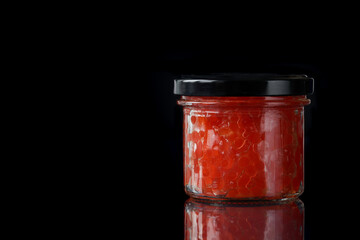Closed glass jar with red salmon caviar. Black background. Free space for an inscription