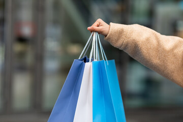 Cropped view of young woman in winter clothes holding bright gift bags outdoors, shopping for cold season, closeup