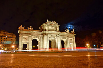 Obraz premium Puerta de Alcala at night and full moon. Light trail effect of vehicles passing through Puerta de Alcala at full moon night.