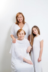 Soft group portrait of women of the same family of different generations in light clothes on a white background.