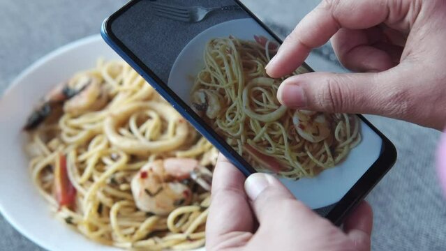 taking picture of plate of sea food pasta with smart phone 