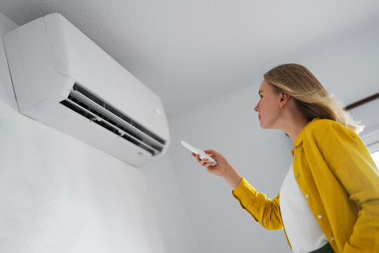 Woman holding remote control aimed at the air conditioner.