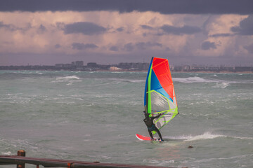 Windsurfer in a wetsuit rushing through the waves against the backdrop of a dark sky and stormy sea