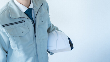 作業服にネクタイの男性。ヘルメットを抱える。建設業イメージ