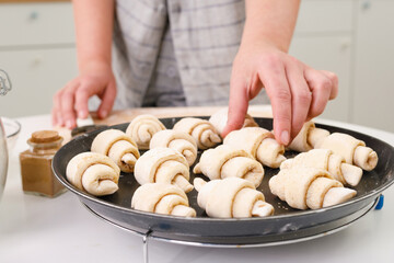 raw mini croissants with cinnamon on a baking tray in a bright home kitchen. Female farts in the frame