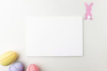 Mockup for Easter holiday greetings with paper rabbit and colorful eggs on a wooden table, top view. Blank template with copy space in minimal style, flat lay.