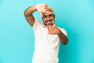 Young Colombian handsome man isolated on blue background focusing face. Framing symbol