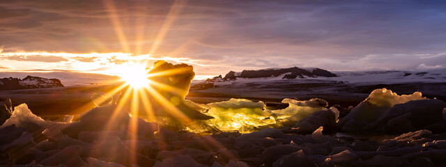 Sunstar forms at the icy edge of an iceberg with a fire sunset over the cold snow ice and rugged...