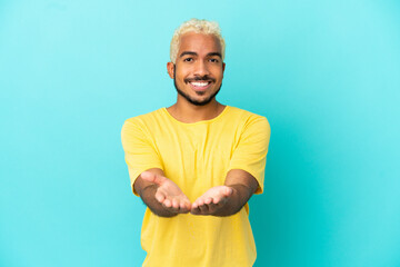 Young Colombian handsome man isolated on blue background holding copyspace imaginary on the palm to...