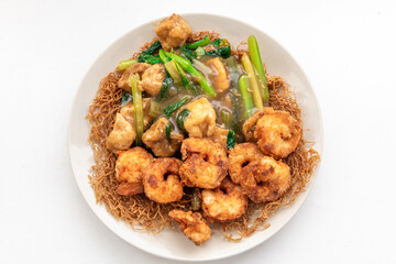 A plate of crispy toasted noodles with fried tofu, king prawns and seasonal green vegetable.