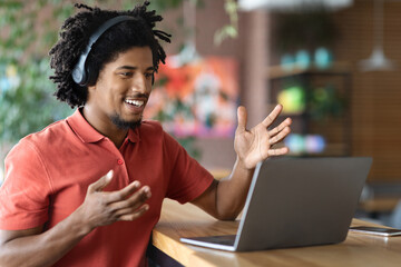 Young Black Man Wearing Headphones Making Video Call With Laptop In Cafe