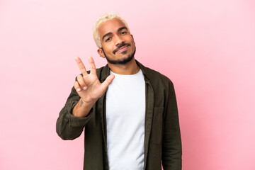 Young Colombian handsome man isolated on pink background happy and counting three with fingers