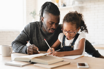 Fototapeta Tutoring homeschooling concept. African father dad childminder helping daughter student with homework, drawing together, e-learning, preparing for school art project at home. obraz