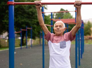 Obraz premium Senior man hanging from pullup bar outoors