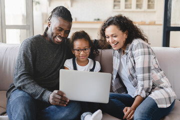 Smiling happy african-american family, mother and father parents with preteen daughter using laptop...
