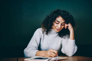 Intelligent Middle Eastern student writing information in education notepad learning at table desktop, young woman with textbook for planning making notes while doing homework and studying indoors