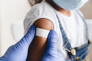 Covid 19 measles, ebola vaccinated. Doctor pediatrician injecting making vaccine to little african girl in medical clinic. Nurse applying medical patch after injection - obrazy, fototapety, plakaty