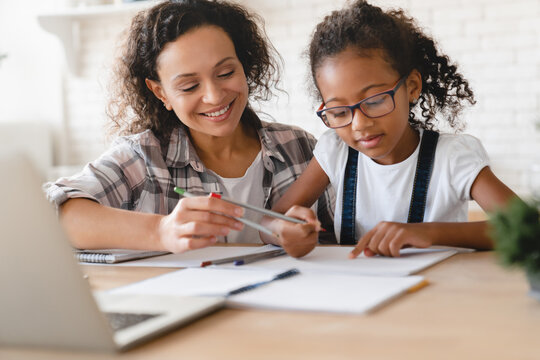 African-american mom mother tutor nanny childminder drawing together helping assisting with homework school project to a preteen daughter. Homeschool concept. E-learning on laptop