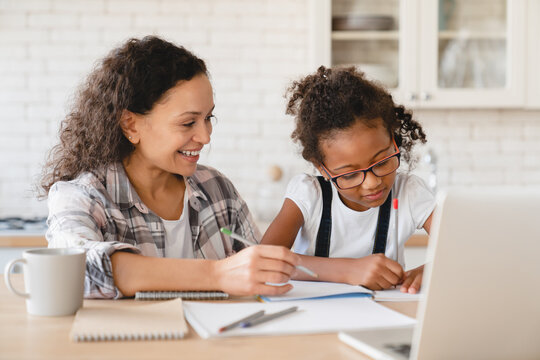 Tutoring homeschooling concept. African mother mom nanny childminder helping daughter with homework, drawing together, e-learning, preparing for school art project at home.