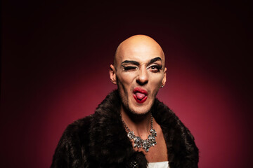Portrait of gender fluid middle-aged transgender gay man with shaved head winking, showing tongue...