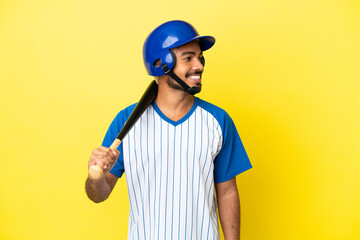 Young Colombian latin man playing baseball isolated on yellow background looking side