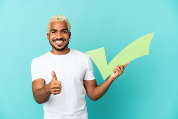 Young Colombian handsome man isolated on blue background holding a check icon with thumb up