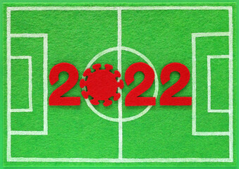 Red felt new year numbers 2022, zero in the form of a corona virus, placed on mini football field made of green felt, top view. Concept about soccer championship during covid pandemic. - obrazy, fototapety, plakaty
