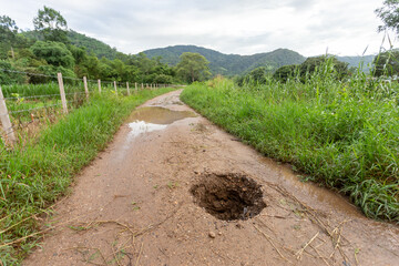 Fototapeta na wymiar big hole on the ground country road due to broken pipes under the road See the dangers of traveling on broken paths. Roads are often damaged during the rainy season.