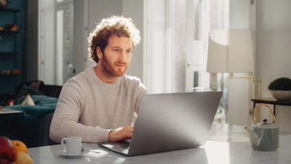 Handsome Adult Man with Ginger Curly Hair Using Laptop Computer, Sitting in Living Room in...