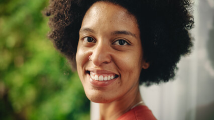 Close Up Portrait of a Happy Young Latina with Brown Eyes, Afro Hair and Nose Piercing Posing for Camera. Beautiful Diverse Multiethnic Black Hispanic Female Smiling on Green Nature Background.