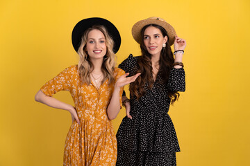 beautiful women friends together isolated on yellow background in black and yellow dress and hat