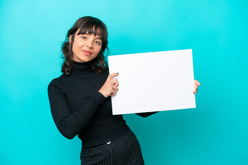 Young latin woman isolated on blue background holding an empty placard with happy expression