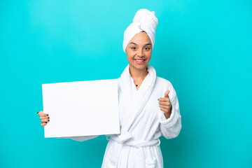 Young woman in a bathrobe with towel isolated on blue background holding an empty placard with thumb up