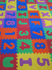 Foam colorful puzzle pieces. Children's play rubber floor background. Texture of colored rubber pieces with numbers and letters for learning and fun. Alphabet and Number Blocks.