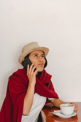 Latin peasant woman wearing hat and a red shawl seated drinking a cup of coffee while listening to...