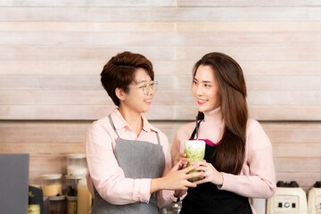 Portrait Asian positive young bearded and beautiful attractive women barista couple smile and enjoy working together at the modern coffee shop. Digital marketing and Coffee Business Concept.