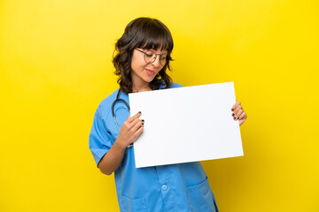 Obraz na płótnie Canvas Young nurse doctor woman isolated on yellow background holding an empty placard with happy expression