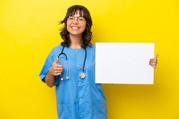 Young nurse doctor woman isolated on yellow background holding an empty placard with thumb up