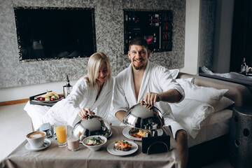 A married couple have breakfast in bed. Hotel room.
