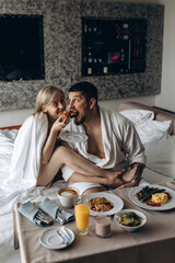 A married couple have breakfast in bed. Hotel room.