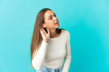 Young woman over isolated blue background listening to something by putting hand on the ear