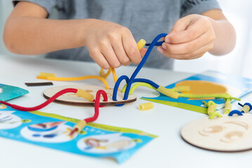 development of fine motor skills. Early education, Montessori Method. Cognitive skills, Children development. Close up of child hands playing with lace or rope and pasta
