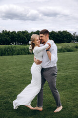 The newlyweds frolic barefoot on a green meadow. Summer day.