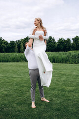 The newlyweds frolic barefoot on a green meadow. Summer day.