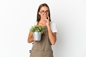 Gardener girl holding a plant over isolated white background thinking an idea while looking up