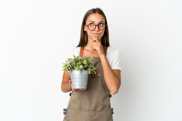 Gardener girl holding a plant over isolated white background having doubts and thinking