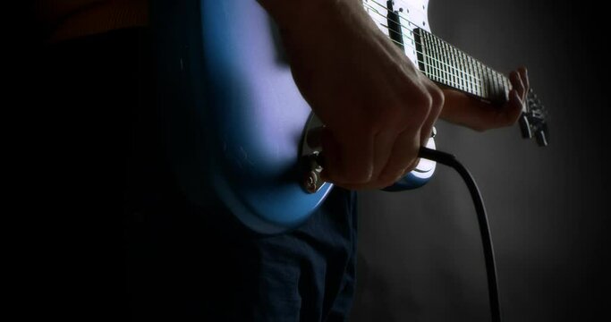 Male guitarist plug in electric guitar. Creative musician playing fingerpicking with a mediator on a blue electric guitar. Black background. High-quality 4K video. Shot with RED camera. Slow motion.