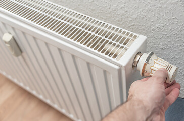 House heating battery with maximum heating power setting and man hand is adjusting its dial. Concept of energy consumption in households.
