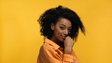 young and cheerful african american woman with curly hair isolated on yellow.