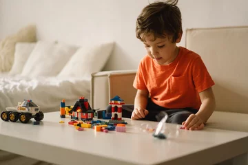 Fotobehang Lego Cute boy is playing constructor at home. Kid playing block toys in home at nursery. Toddler having fun and building out of bright constructor bricks. Development and Construction Concept  © Анастасія Стягайло